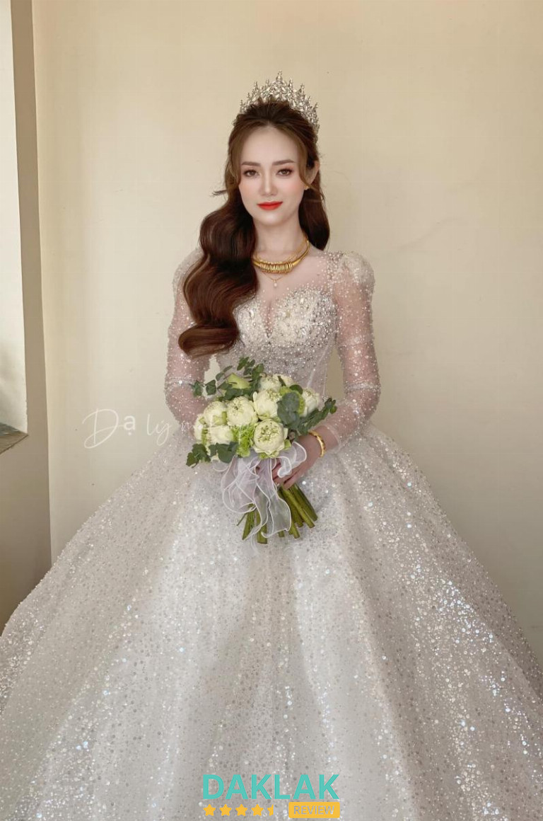 Váy cưới công chúa phủ sequin lấp lánh, tay dài xuyên thấu, cô dâu cầm bó hoa trắng trong bối cảnh studio Dạ Lý.