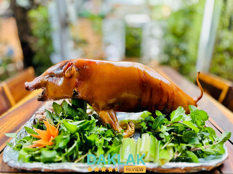 “Món heo rẫy nướng nguyên con, da vàng giòn, bày trên mâm kèm rau rừng và củ quả tươi tại Buôn Ma Thuột.”