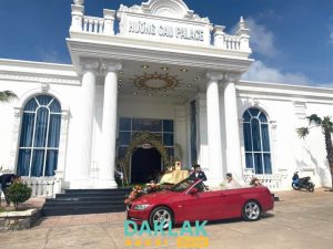 “Mặt tiền Nhà Hàng Hương Cau Palace tại Ea Kar với kiến trúc trắng sang trọng, cổng lớn và xe hoa đón dâu trước sảnh.”