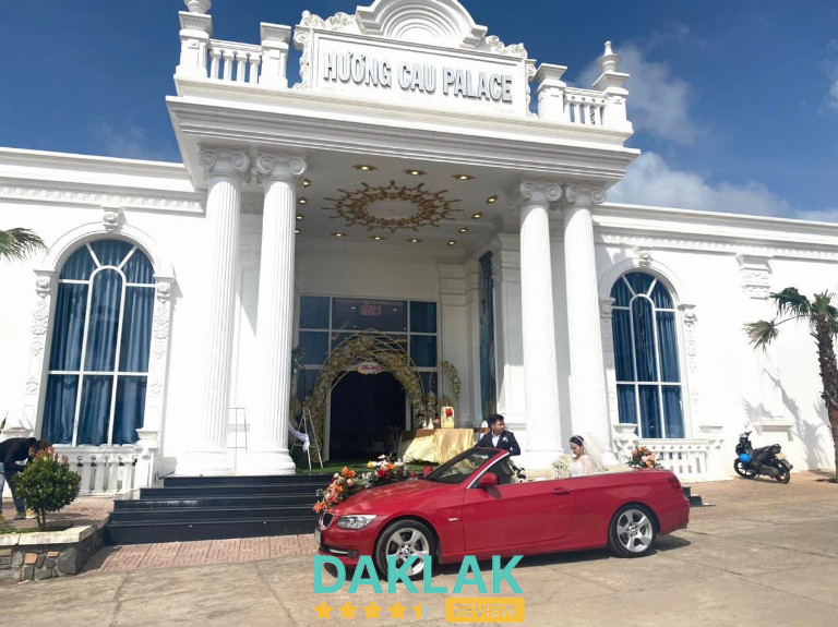 “Mặt tiền Nhà Hàng Hương Cau Palace tại Ea Kar với kiến trúc trắng sang trọng, cổng lớn và xe hoa đón dâu trước sảnh.”