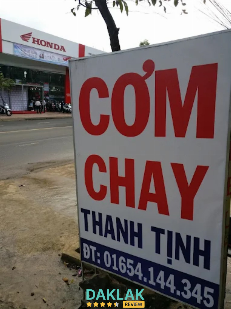 “Biển hiệu quán Cơm Chay Thanh Tịnh đặt bên lề đường quốc lộ, nền trắng chữ đỏ – xanh nổi bật, phía sau là đại lý Honda.”