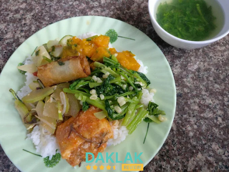 Đĩa cơm chay gồm rau xào, bí đỏ, chả chay, chả giò và chén canh rau xanh đặt trên bàn đá.”