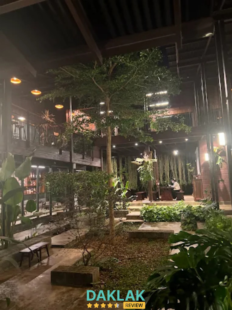 Không gian sân vườn Xã Cafe buổi tối với cây xanh, đèn vàng và khu ngồi yên tĩnh