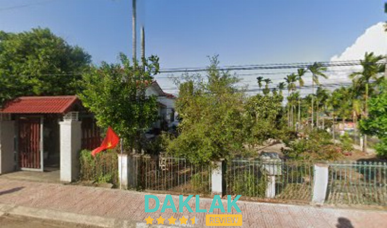 Khu nhà cấp bốn có cổng rào và sân vườn nhiều cây xanh, nhìn từ vỉa hè phía trước